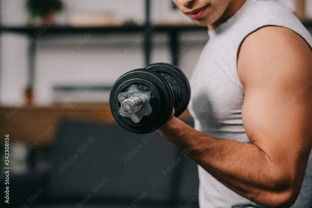 Cropped view of mixed race sportsman training with heavy dumbbell Cropped view of mixed race sportsman training with heavy dumbbell