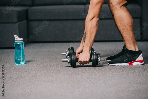 cropped view of sportsman putting dumbbells on floor in living room