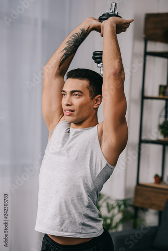 muscular bi-racial man with tattoo workout with dumbbell