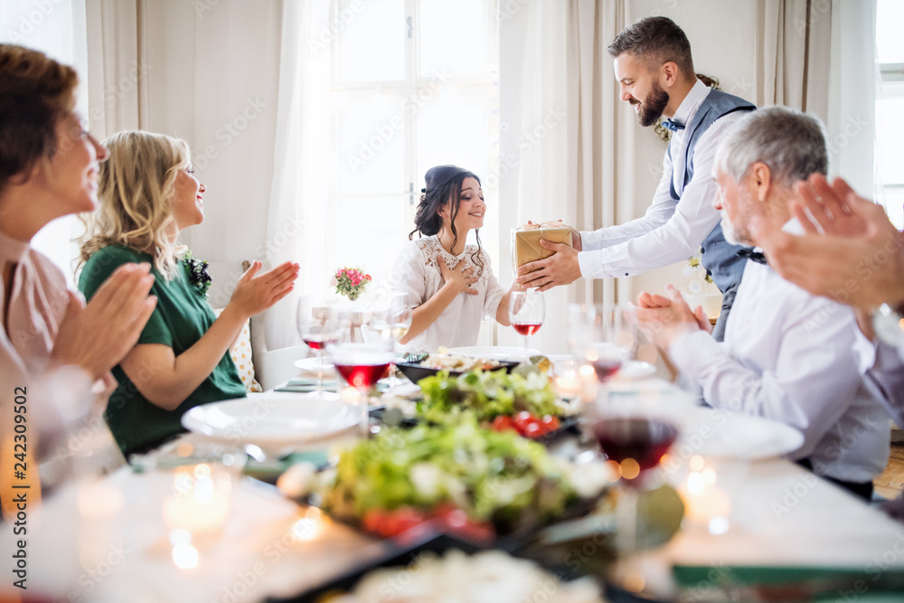 A man giving gift to a young surprised woman on a family birthday party.