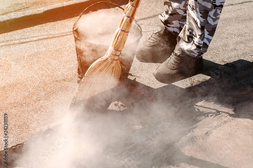 Worker repairs the roof with molten tar from a bucket with a broom. Roof repair tar.