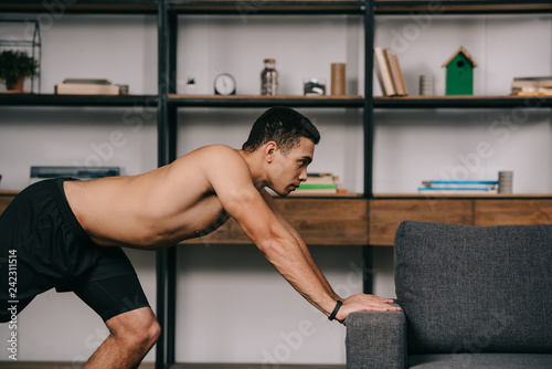 strong mixed race man workout near sofa in living room