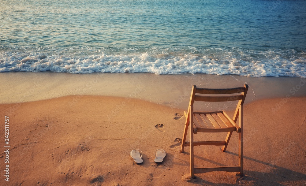 White sandals and wooden chairs placed on the sand with blue waves ocean. White sandals and wooden chairs placed on the sand with blue waves ocean.
