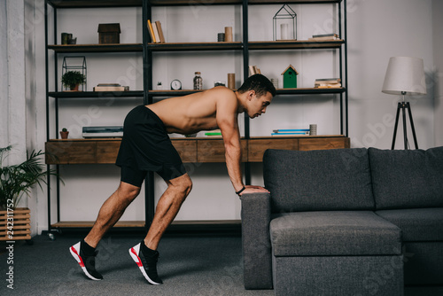 muscular mixed race man exercising near sofa in living room