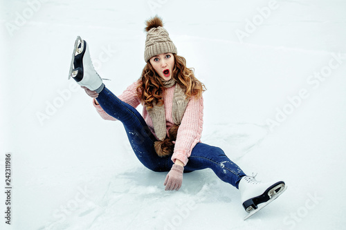 Beautiful girl in warm clothes sitting on ice rink after falling and laughing photo