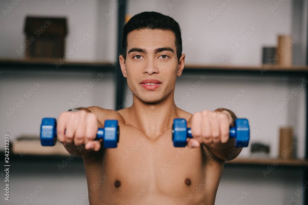 selective focus of bi-racial man exercising with blue dumbbells selective focus of bi-racial man exercising with blue dumbbells