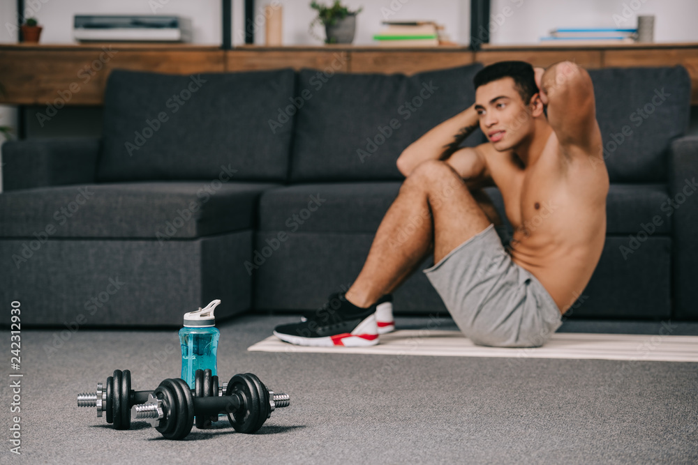Obraz premium selective focus of dumbbells near sport bottle with bi-racial man on background