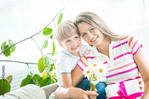 Mother and son together closeup portrait. Mothers day picture with copy space. Family indoors happy. Smiling mom with her child holding present and flowers.