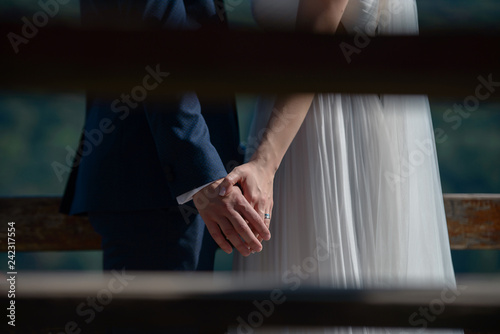 Cropped, paparazzi-style, private shot of young Caucasian bride wearing a silky white dress and groom in a dark blue suit holding hands, beautiful couple having a moment of intimacy before the wedding