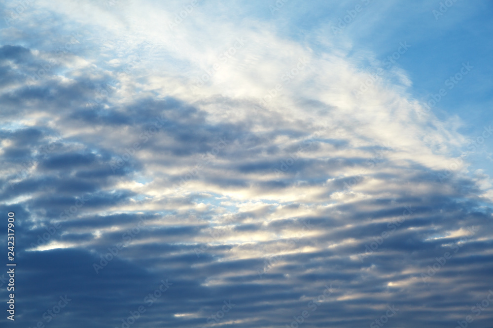 Fototapeta premium feathery clouds in the blue sky are illuminated by the rays of the sun, setting over the horizon