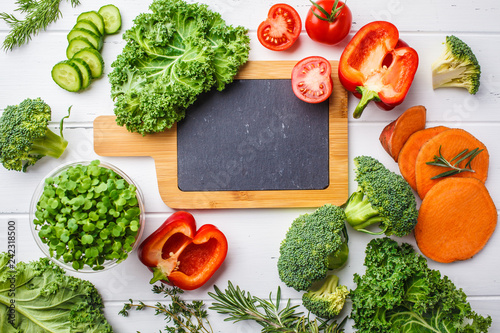 Fresh ingredients  kale  sweet potatoes  tomatoes  broccoli  peppers and sprouts  for cooking salad on white wooden background  slate board for text  top view.