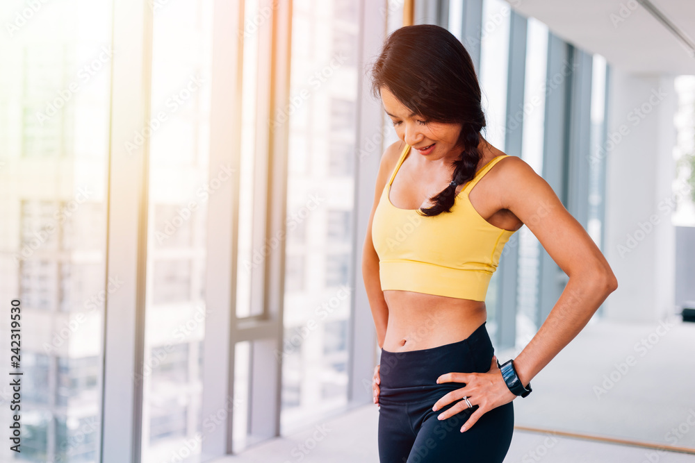 Portrait of young fit Asian woman standing in gym, hands on hips pose. Fitness female model image