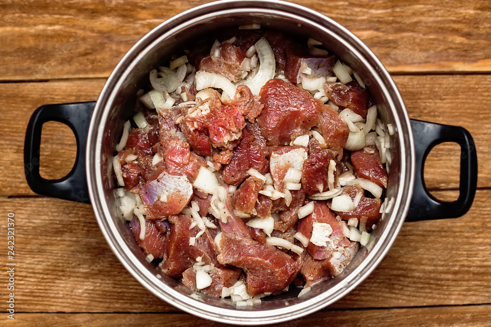 Marinated meat pieces with onions in pan on wooden background. Preparation of raw meat for barbecue. The view from the top. Raw beef mixed with onions and spices. Marinated meat pieces with onions in pan on wooden background. Preparation of raw meat for barbecue. The view from the top. Raw beef mixed with onions and spices.