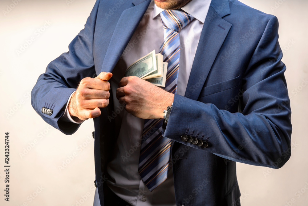 A man in an expensive suit puts money in the inside pocket of his jacket.  Concept on the topic of corruption. Stock Photo