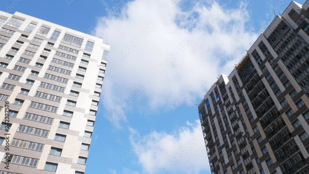 Low angle shot of new-built block of flats and unfinished apartment house against the blue sky with white clouds. Housing development Low angle shot of new-built block of flats and unfinished apartment house against the blue sky with white clouds. Housing development