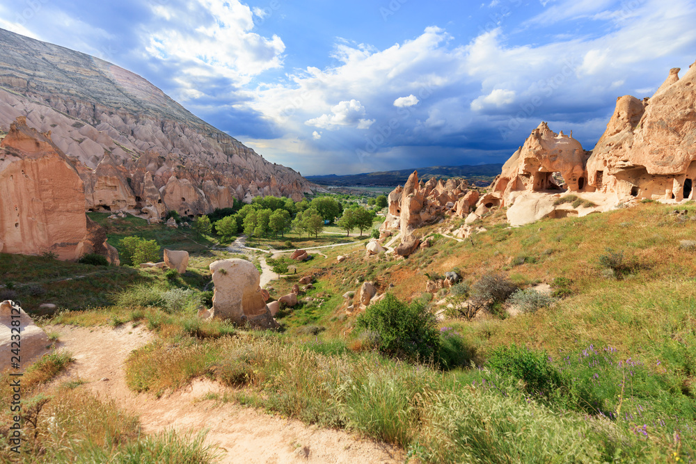 Obraz premium Droga gruntowa wije się między stożkowymi szczytami skał, starożytnymi jaskiniami na tle górskiego krajobrazu doliny w Kapadocji