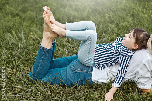 Horizontal side view of beautiful woman lying and playing with her cute little girl on the green grass outdoors. Happy child and mother spend time together in the park. Mother's day concept