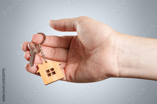 Hand of a real estate agent holding a house key on grey background