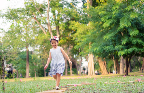 5 years old cute little girl playing in sunny summer park.Happy kid girl walking and jumping in a forest.Kids play outdoors.Kindergarten in school yard on summer day. 