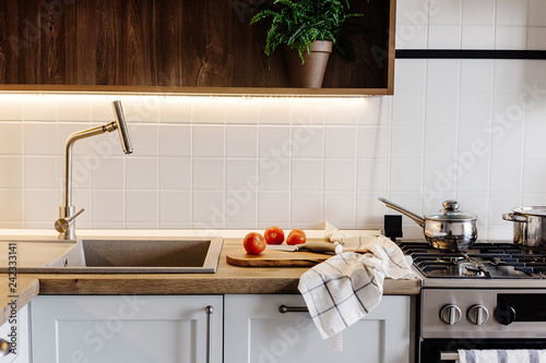 Cooking food on modern kitchen with steel oven, pots, knife on wooden cutting board with vegetables  on wooden tabletop at sink with water. Home food. Stylish kitchen furniture in grey color