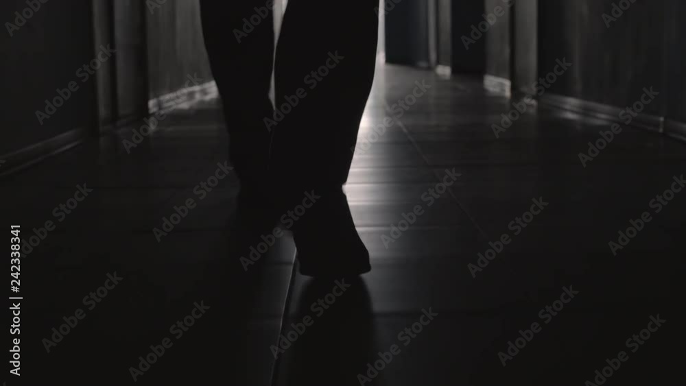 Dolly with low-section of silhouette of legs of man walking along hallway towards the camera