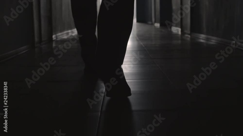 Dolly with low-section of silhouette of legs of man walking along hallway towards the camera