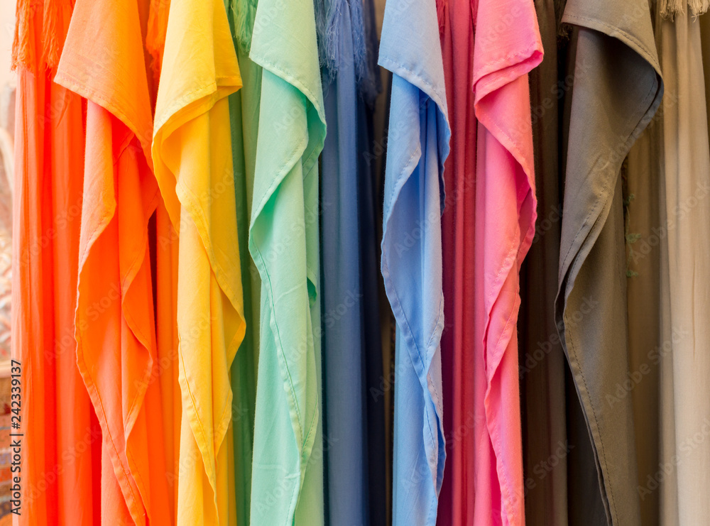 Fashion clothes on clothing rack - bright colorful closet. Close-up of rainbow color choice of trendy female wear on hangers in store closet or spring cleaning concept. Summer home wardrobe.