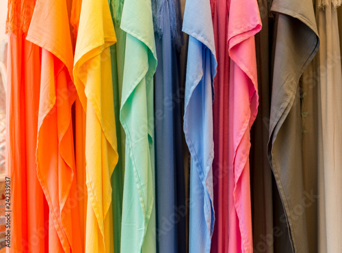 Fashion clothes on clothing rack - bright colorful closet. Close-up of rainbow color choice of trendy female wear on hangers in store closet or spring cleaning concept. Summer home wardrobe.