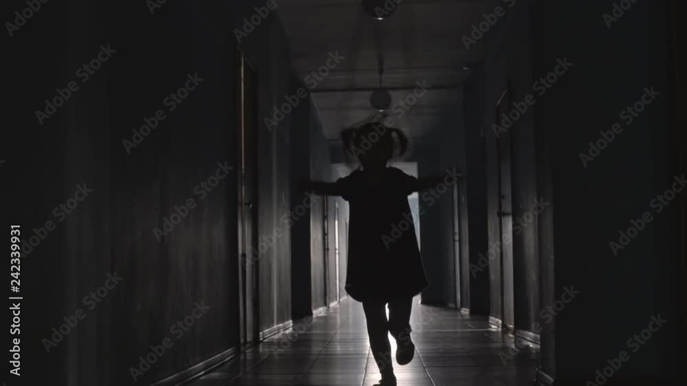 Silhouette of playful little girl with two ponytails jumping the rope towards the camera along hallway