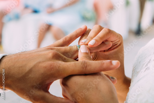 close up of couple of young newly weds with woman hands putting gold wedding ring in husband fingers in summer day