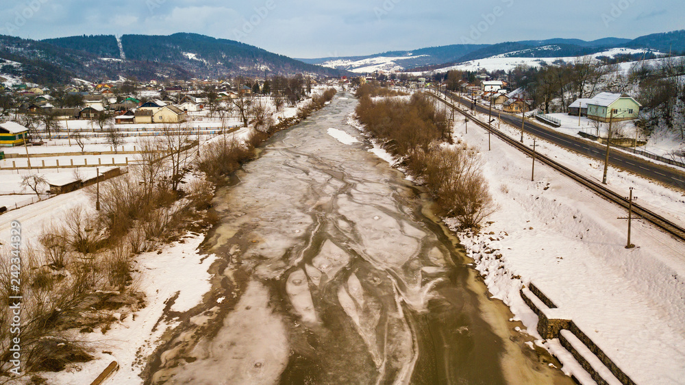 Aerial rural view of snowy river, village, road and railway