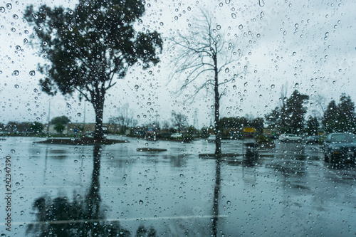 Drops of rain on the window; blurred trees in the background; shallow depth of field