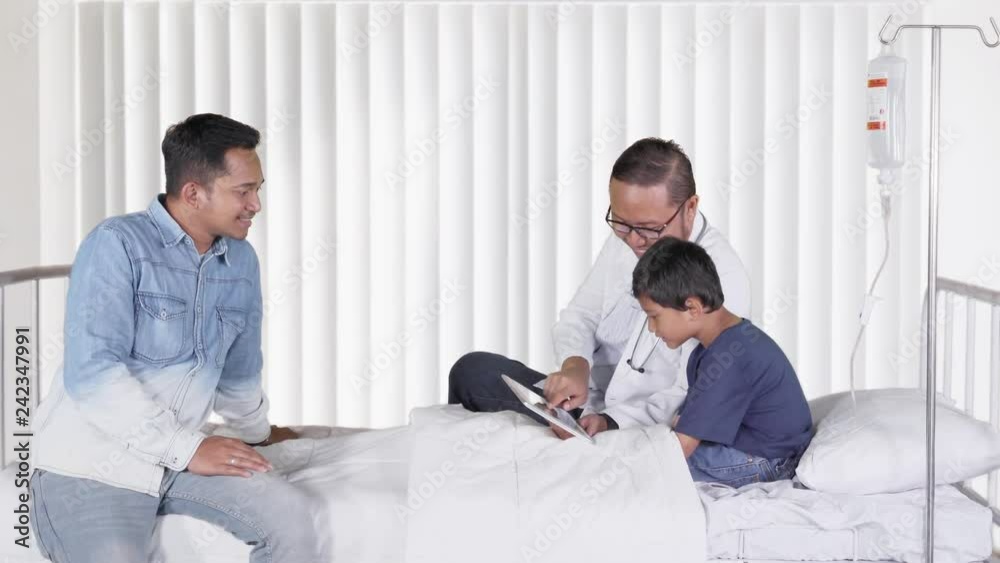 Young male doctor explaining medical record on sick little boy patient while sitting on the bed in hospital room. Shot in 4k resolution Young male doctor explaining medical record on sick little boy patient while sitting on the bed in hospital room. Shot in 4k resolution