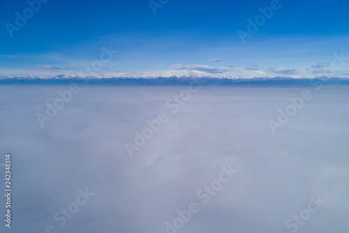 Aerial view, flying over clouds of fog. Panoramic view of the Po Valley (Italy) covered by thick fog with the Alps and the Monte Rosa group in the background. © Arcansél