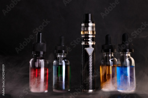 Electronic cigarette and bottles with vape liquid within vapor on black background