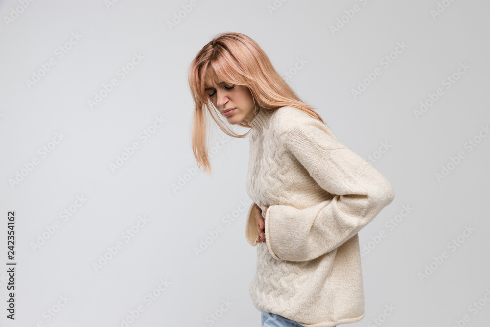 Young cute woman in white sweater suffering from stomach ache, having menstruation pain, feels bad, abdominal cramps, side view. Menstrual period, gynecology, gastritis, healthcare, medical concept. Young cute woman in white sweater suffering from stomach ache, having menstruation pain, feels bad, abdominal cramps, side view. Menstrual period, gynecology, gastritis, healthcare, medical concept.