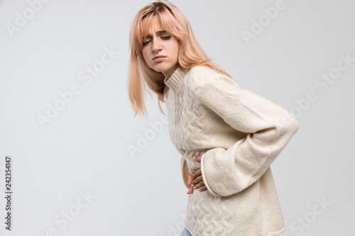 Close up shot of woman in white sweater suffering from stomach ache, having menstruation pain, feels bad, abdominal cramps, side view. Menstrual period, gynecology, gastritis, healthcare concept.