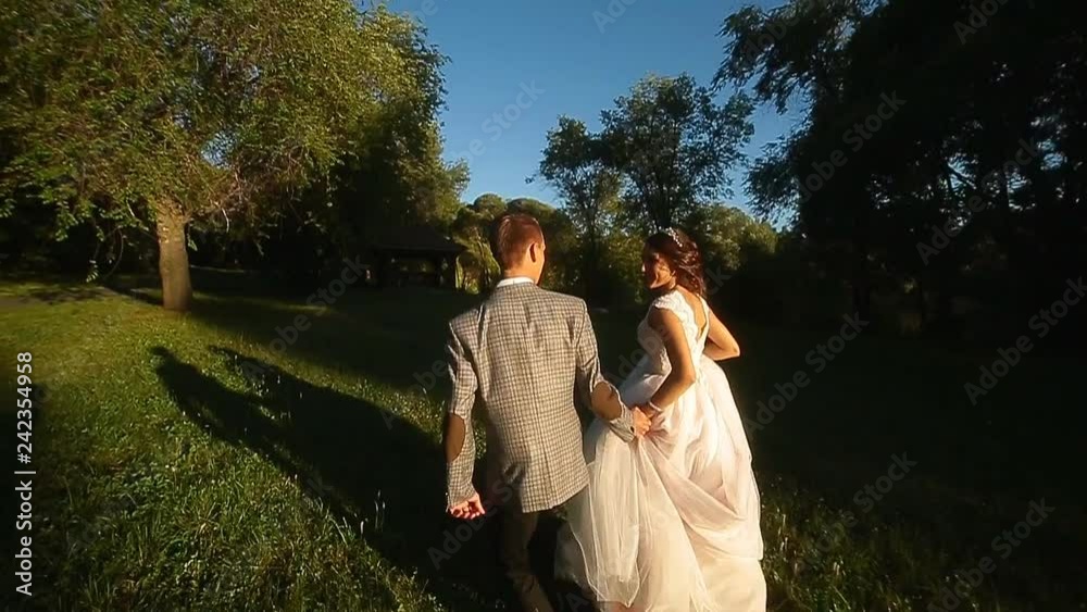 the bride and groom are running along the alley in the park during the summer evening at sunset the bride and groom are running along the alley in the park during the summer evening at sunset
