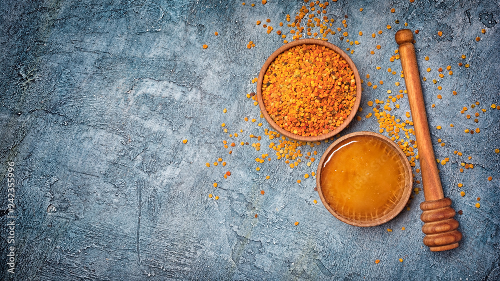 Top view on natural products honey and bee pollen in wooden bowls with honey stick Top view on natural products honey and bee pollen in wooden bowls with honey stick