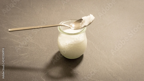 Fett in einem Glasbehälter mit Löffel Kokosöl als Naturkosmetik