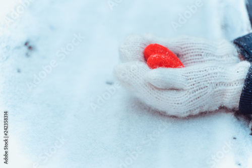 Female hands in knitted white mittens with heart of snow in winter day.