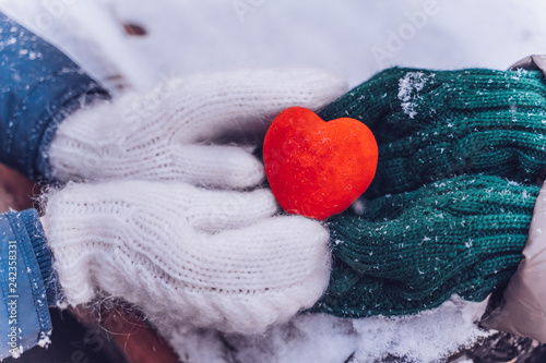 Hands in gloves holding heart closeup on winter snow background. Toned.