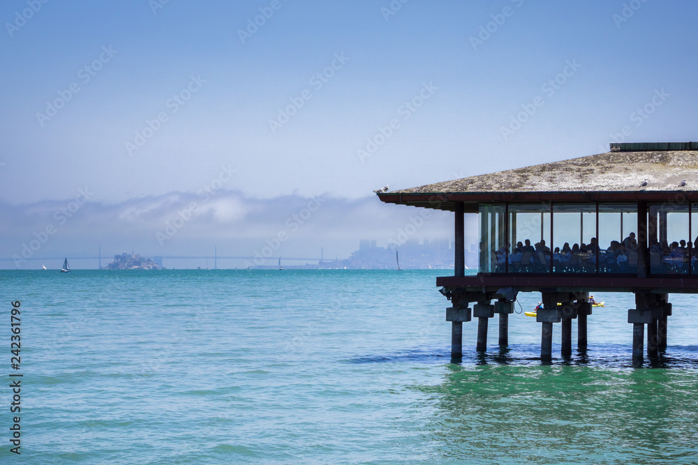 Restaurant on the bay shoreline, San Francisco skyline partially covered by fog in the background; Sausalito, California