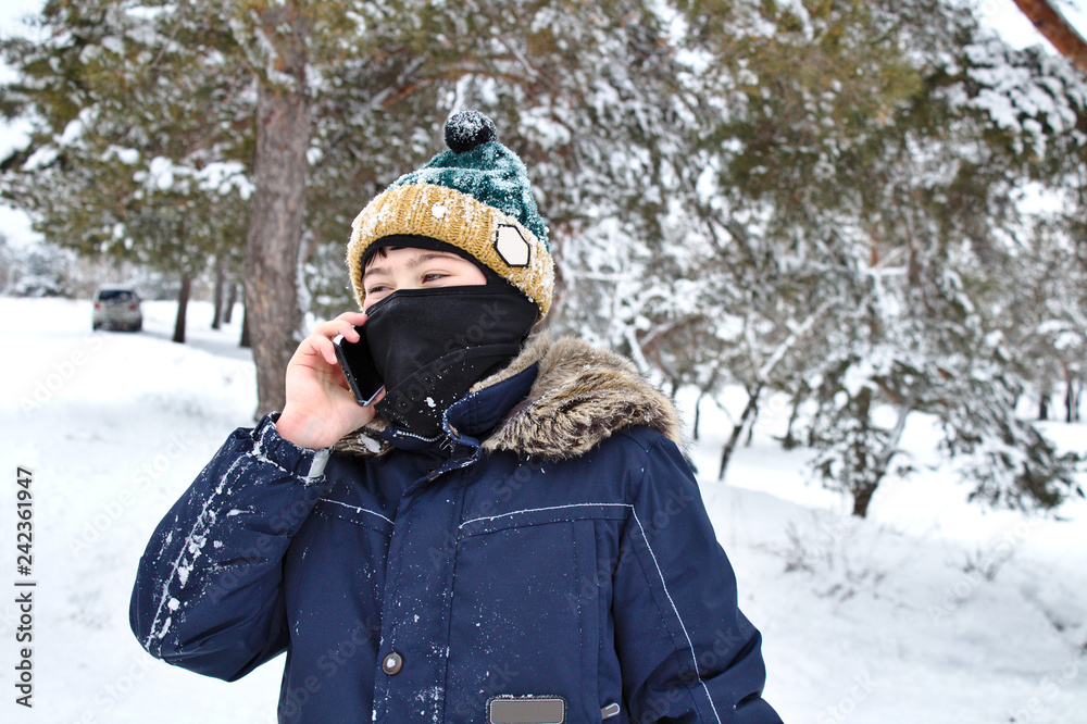 talking on the phone boy in a knitted hat with a bubo and balaclava on a winter walk