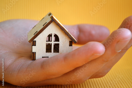 Wooden toy house model in man's hand on yellow background front view