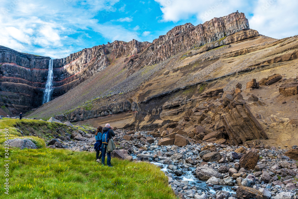 Man and woman tourists enjoying spectacular landscape around of Hengifoss waterfall and basaltic strata with thin, red and yellow layers of clay
