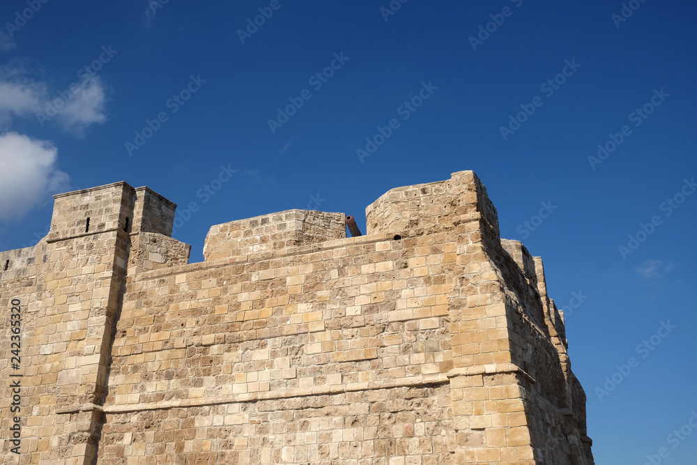 Top section of antique castle wall from old sandy limestone and the cannon on the top under clear blue sky ion sunny day