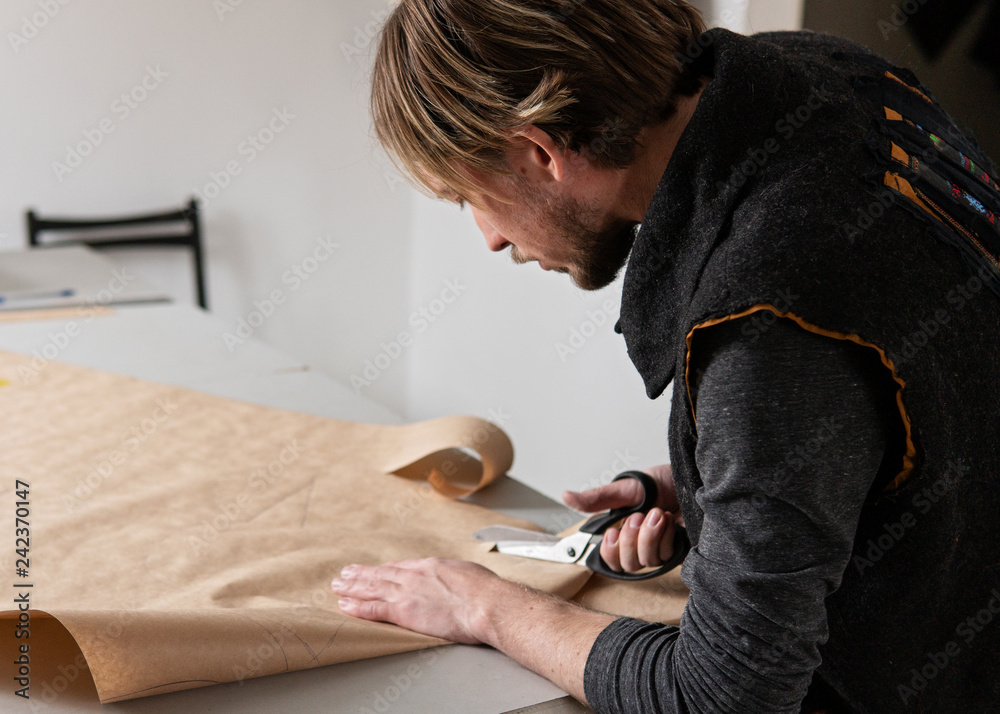 Obraz premium Young man tailor with scissors making clothing pattern