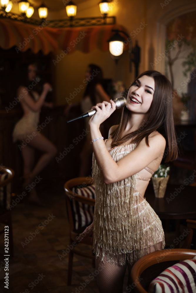 Beautiful young woman singing karaoke songs into the microphone in a restaurant on the background of other girls
