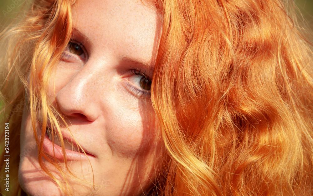 Schönes Portrait in Nahaufnahme einer lächelnden jungen rothaarigen lockigen Frau im Freien